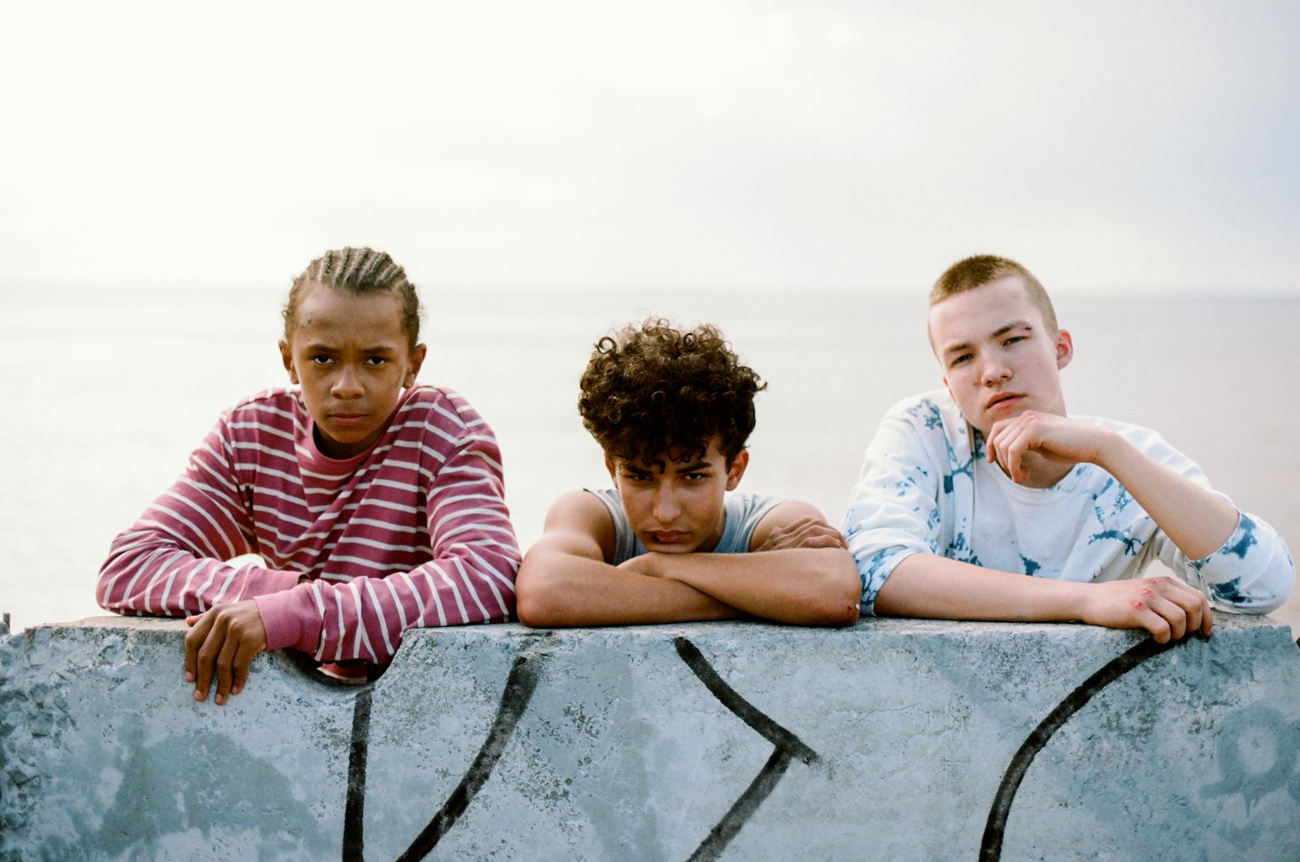A diverse group of teenagers relaxing by a graffitied wall overlooking the ocean.