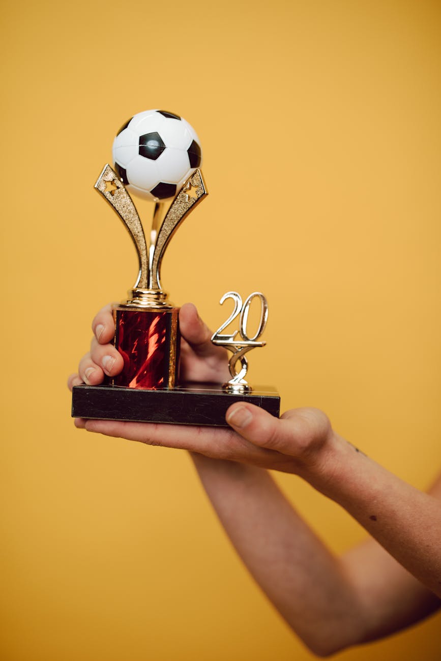 Close-up of hands holding a soccer trophy against a bright yellow backdrop.