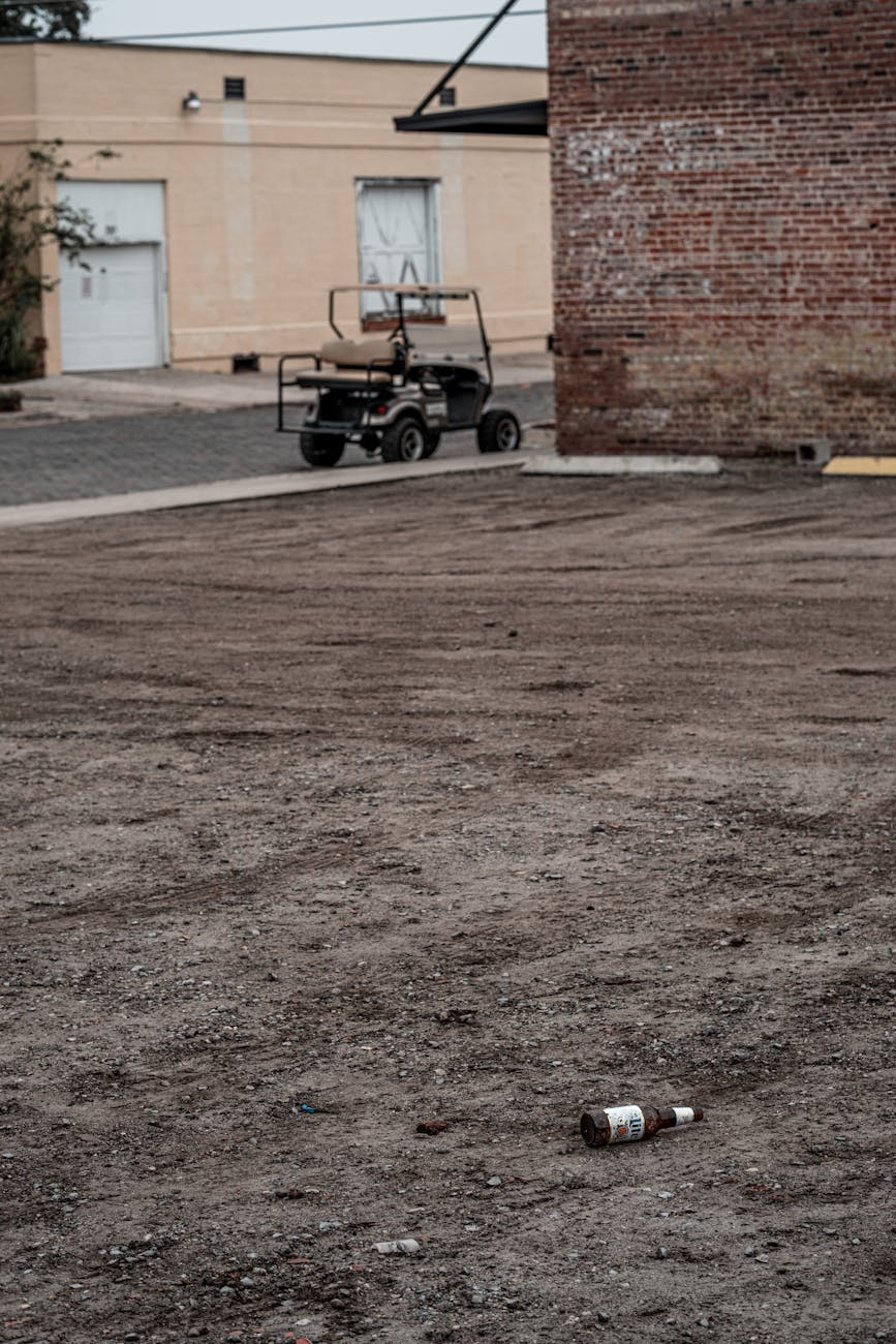 A desolate urban lot with a discarded bottle and an abandoned vehicle.