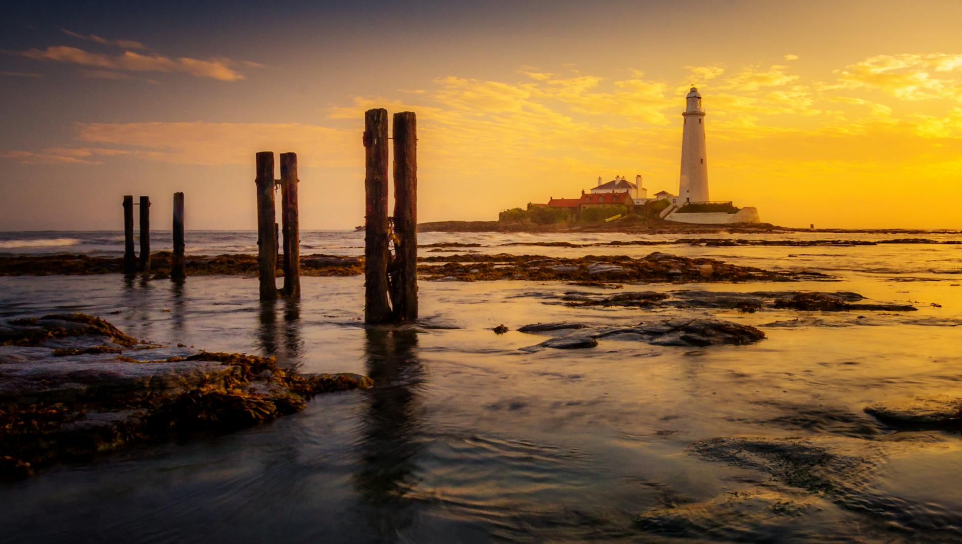 Captivating view of St Mary's Lighthouse at sunset reflecting on the serene sea waters.
