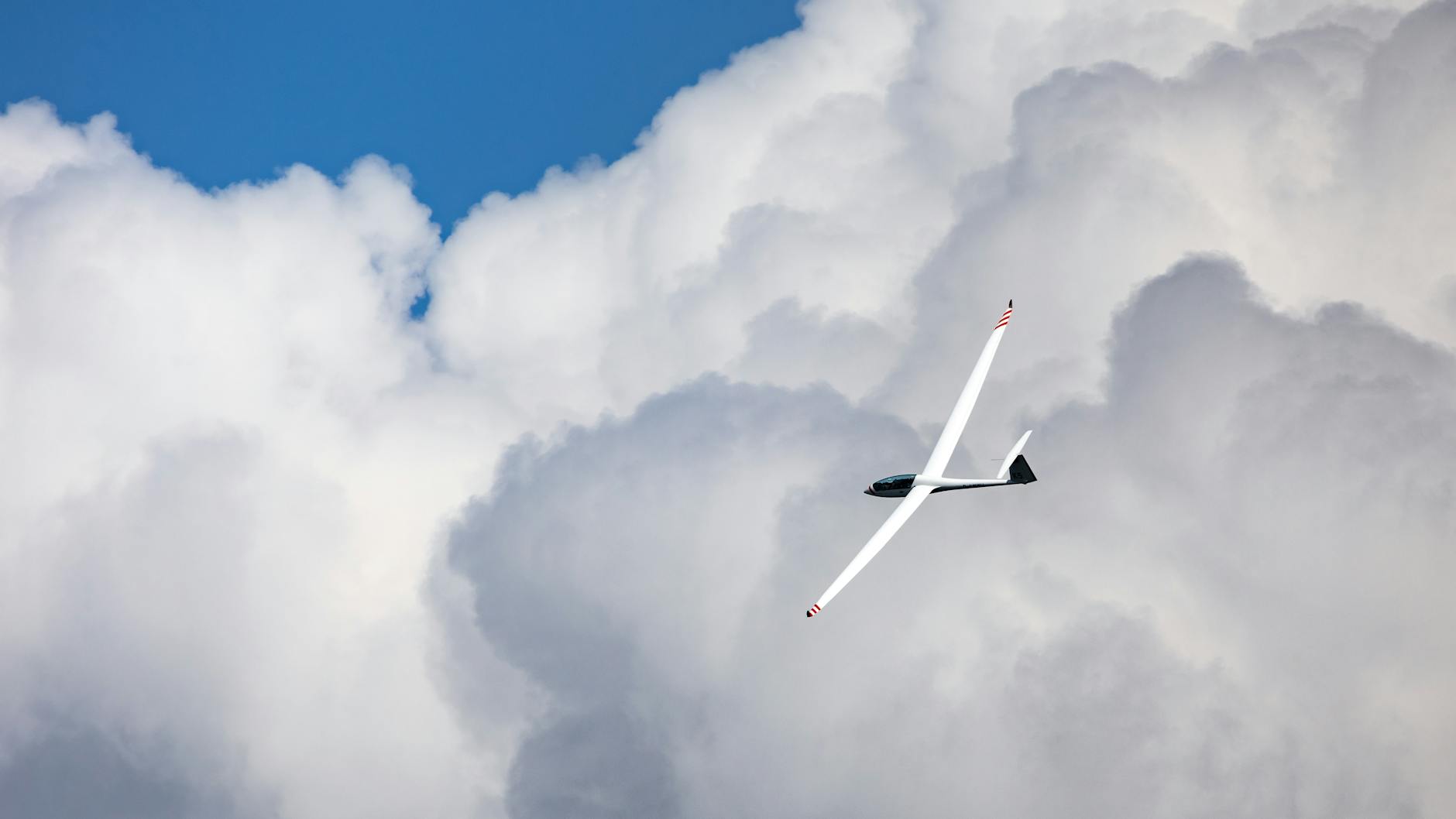 A sleek glider flies gracefully amidst the expansive cumulus clouds under a bright blue sky.