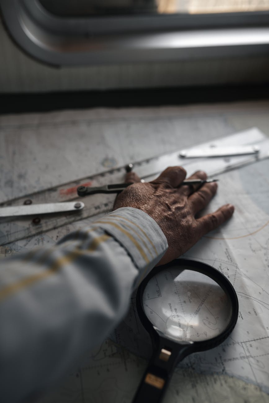 Close-up of a hand using a magnifier and tools on a navigation map, indoors.