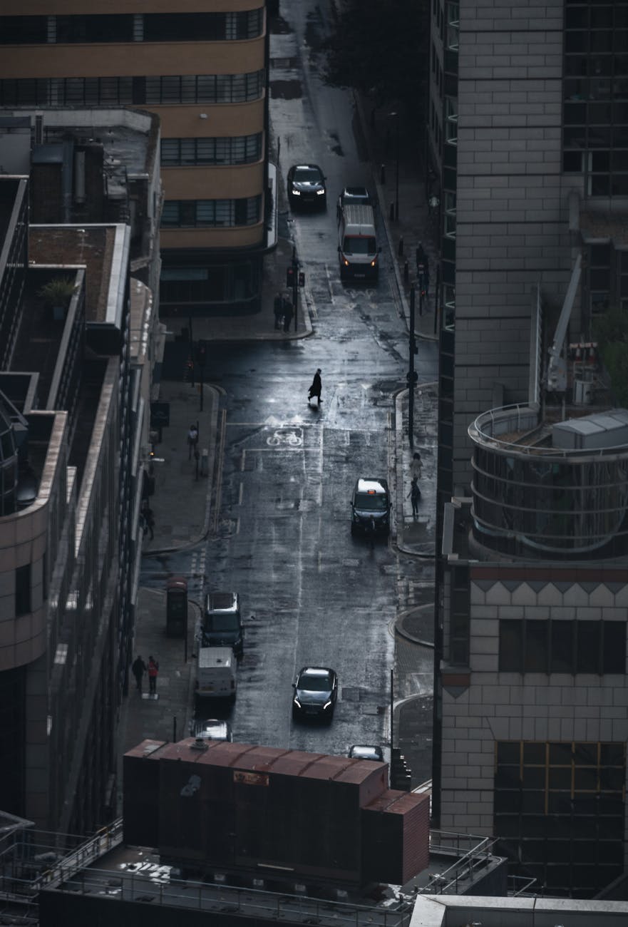 A dark, rainy street view of London with cars and a lone pedestrian under cloudy skies.