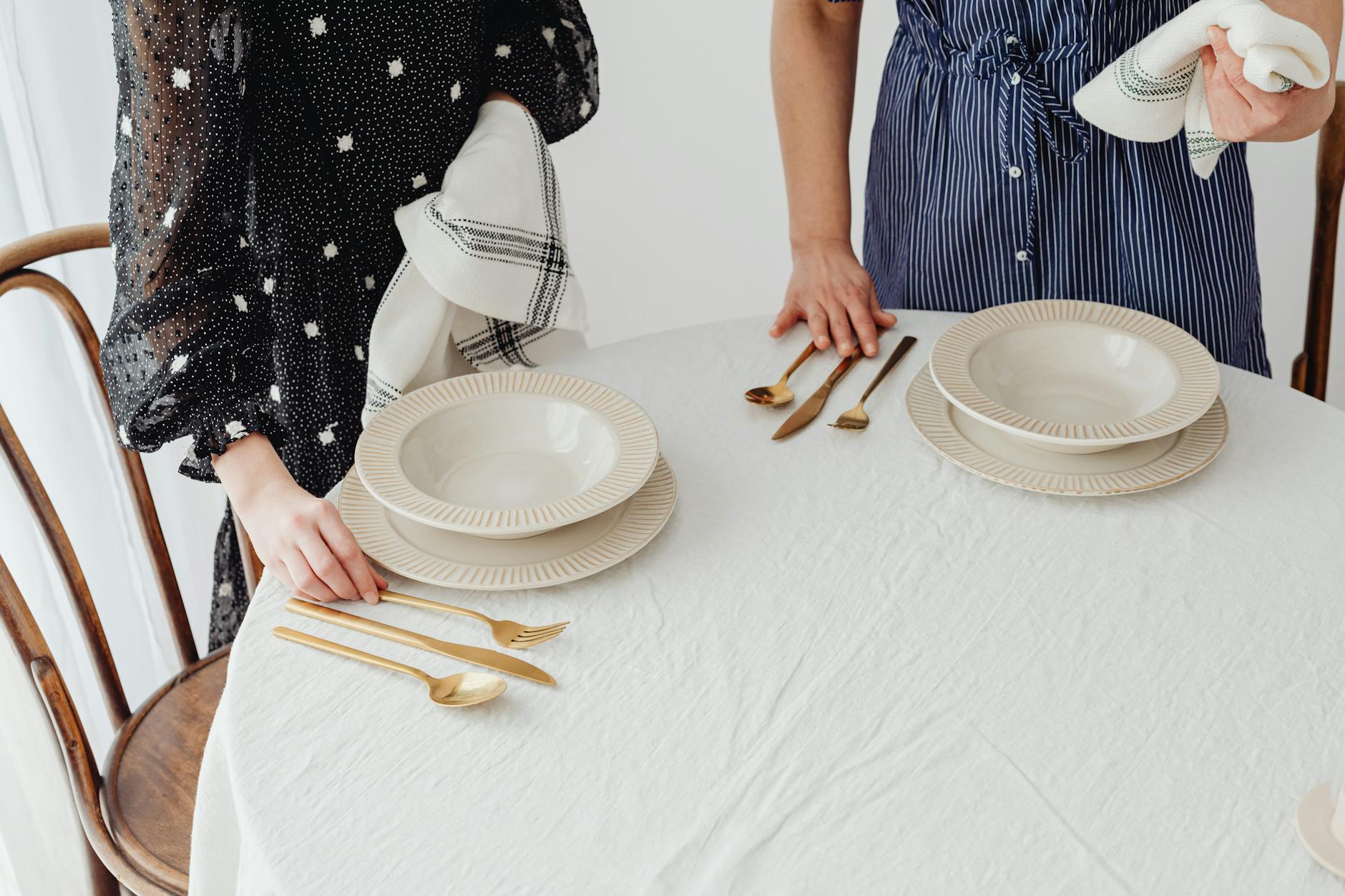 Two people setting a table with ceramic bowls and gold cutlery indoors.